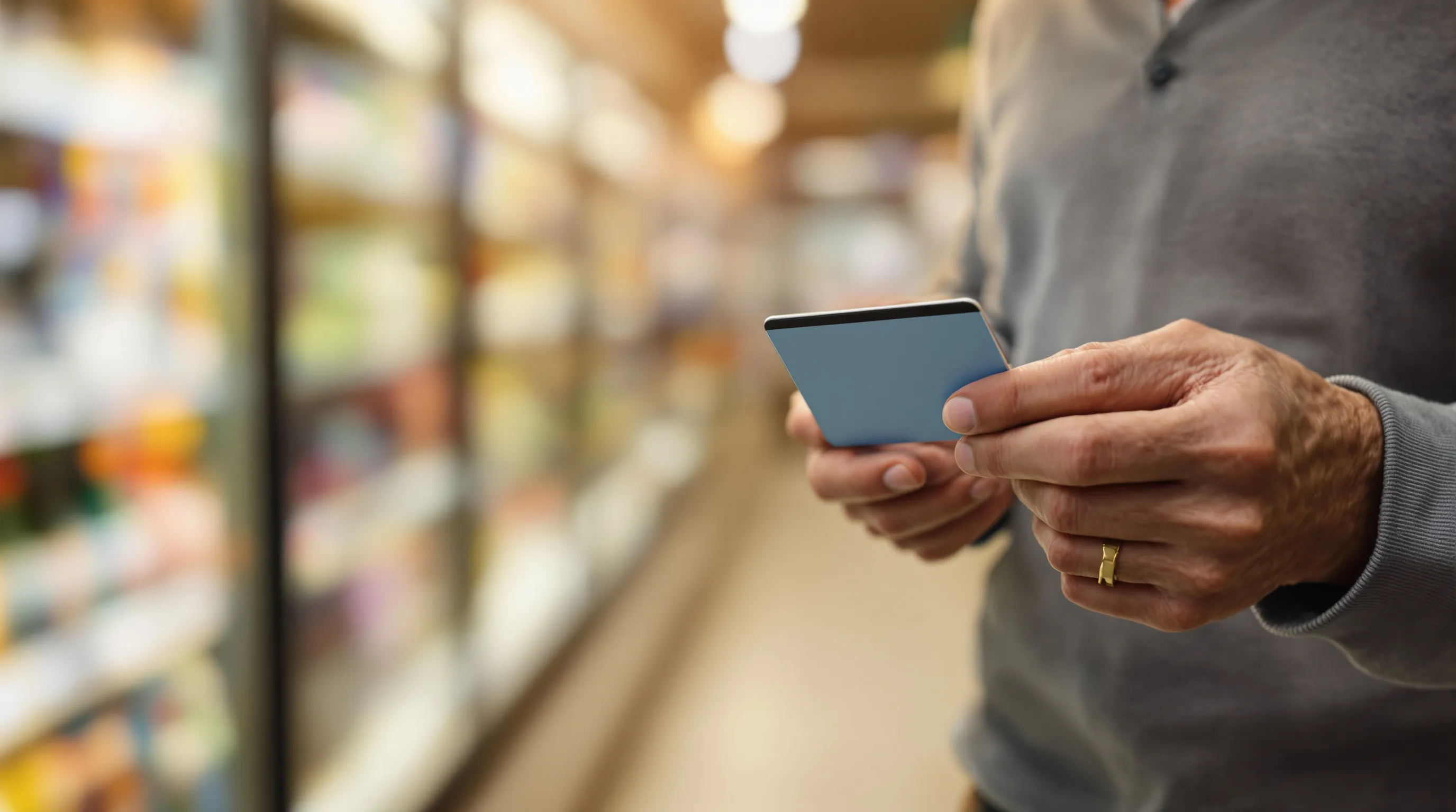 Senior checking Medicare grocery card item eligibility on smartphone app in grocery store aisle